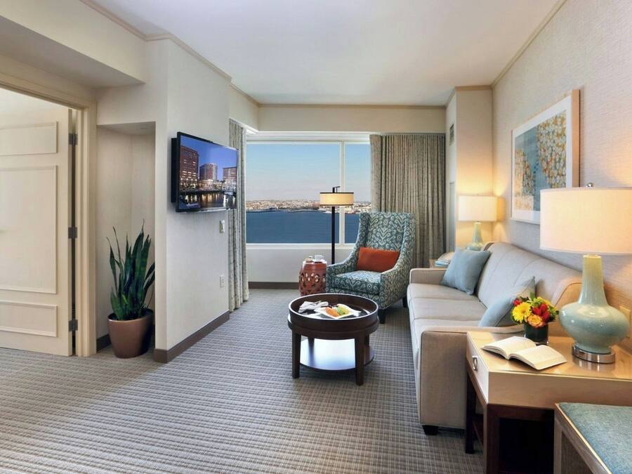 Ein Hotelzimmer mit Sofa, Sessel, Couchtisch, Fernseher und Blick auf die Stadt.