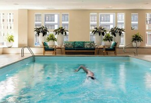 Una piscina interior con una persona nadando, rodeada de amplios ventanales y plantas en macetas.