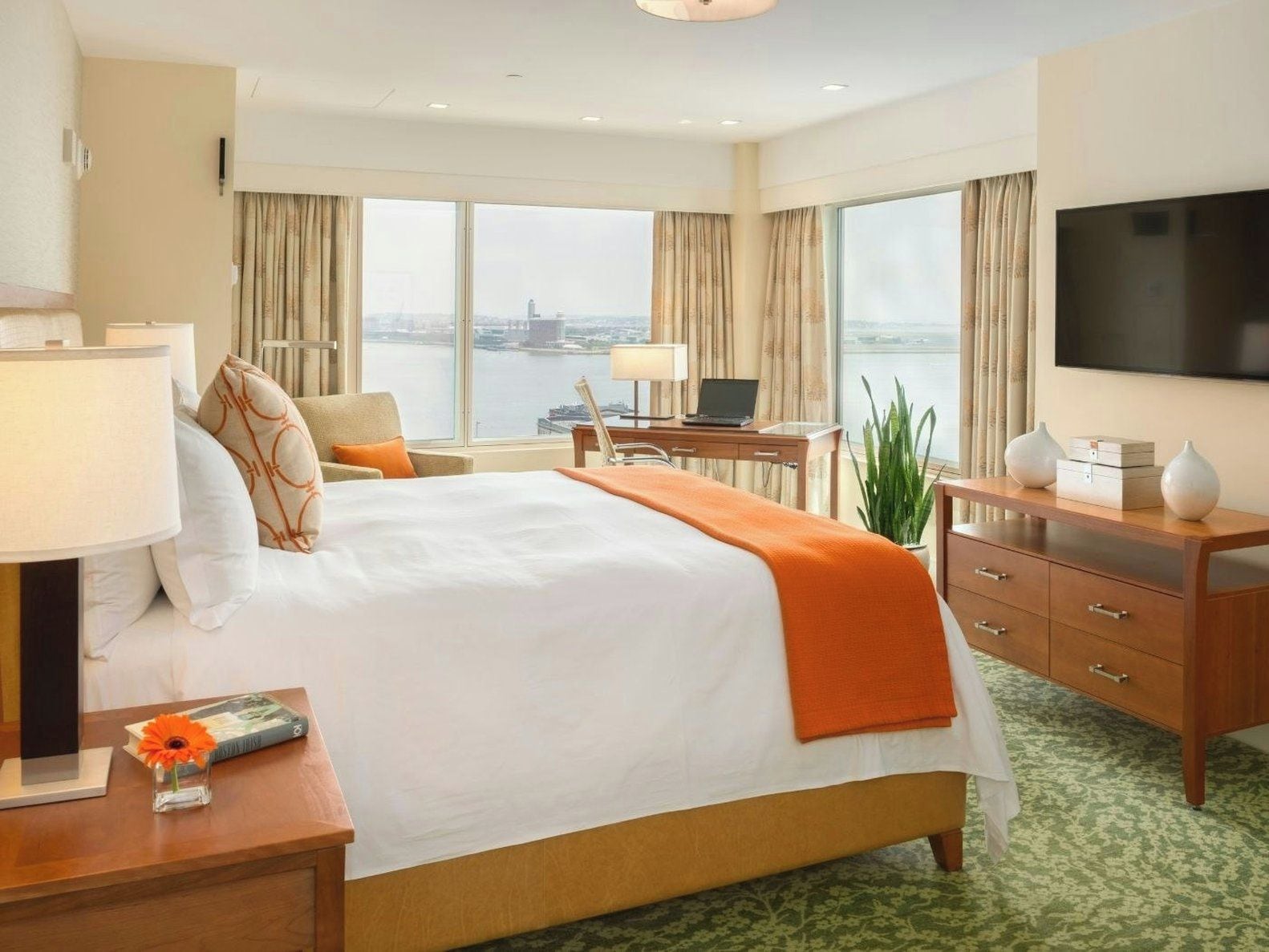 A hotel room with a large bed, a desk, a television, and a view of a cityscape.