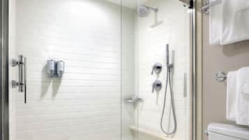Un área de ducha con paredes de azulejos blancos y puerta de cristal, con un inodoro blanco visible a través del cristal.