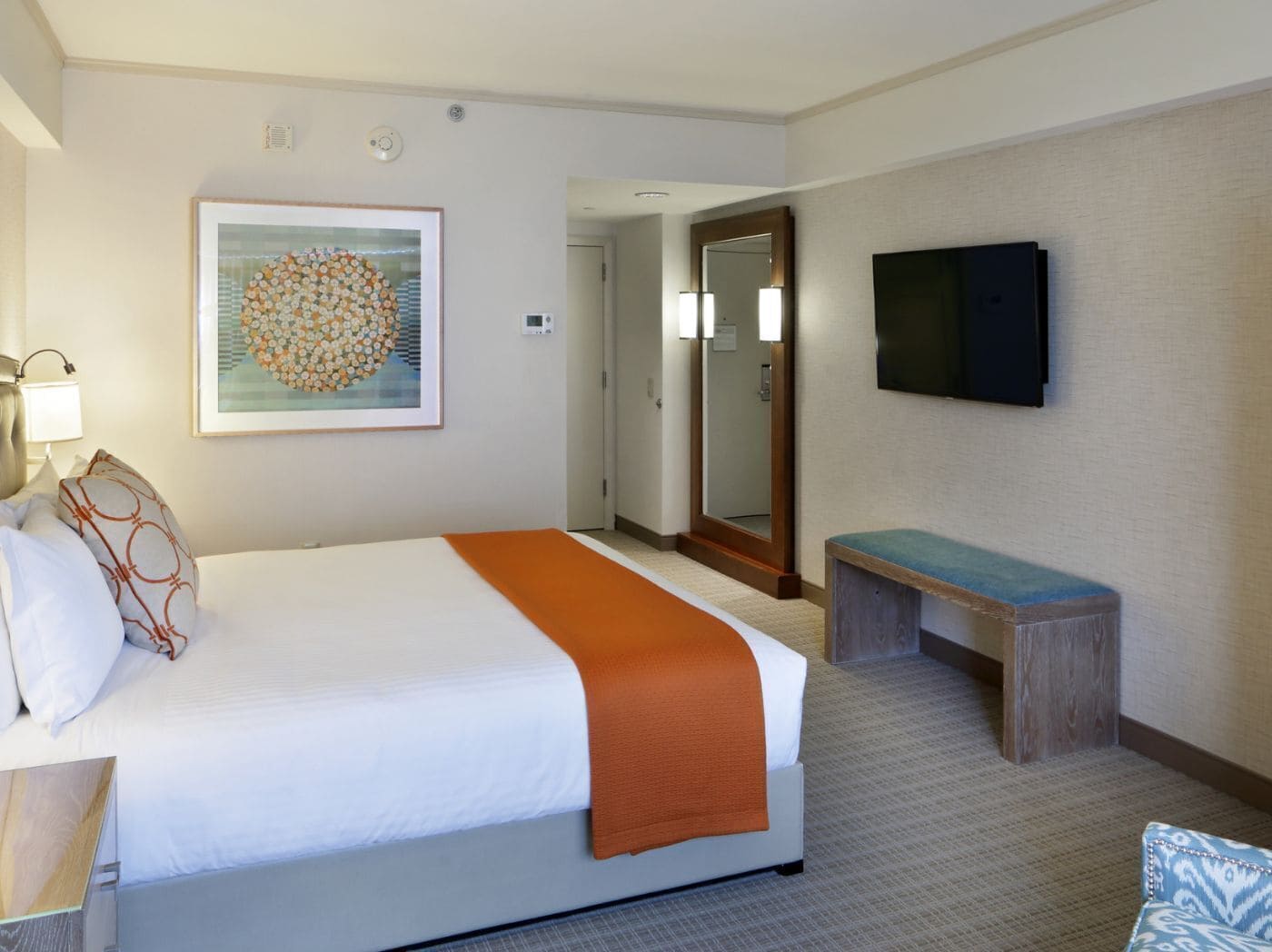 A hotel room with a bed, a bench, a TV, and a framed artwork on the wall.