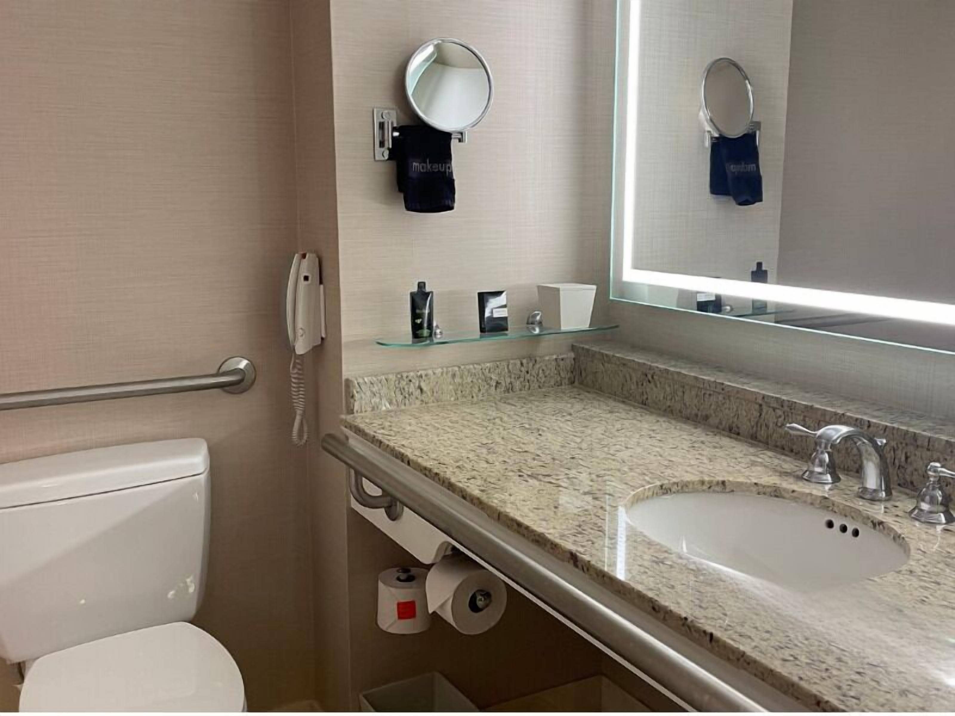 A bathroom with a toilet, sink, mirror, towel rack, and a hand dryer.