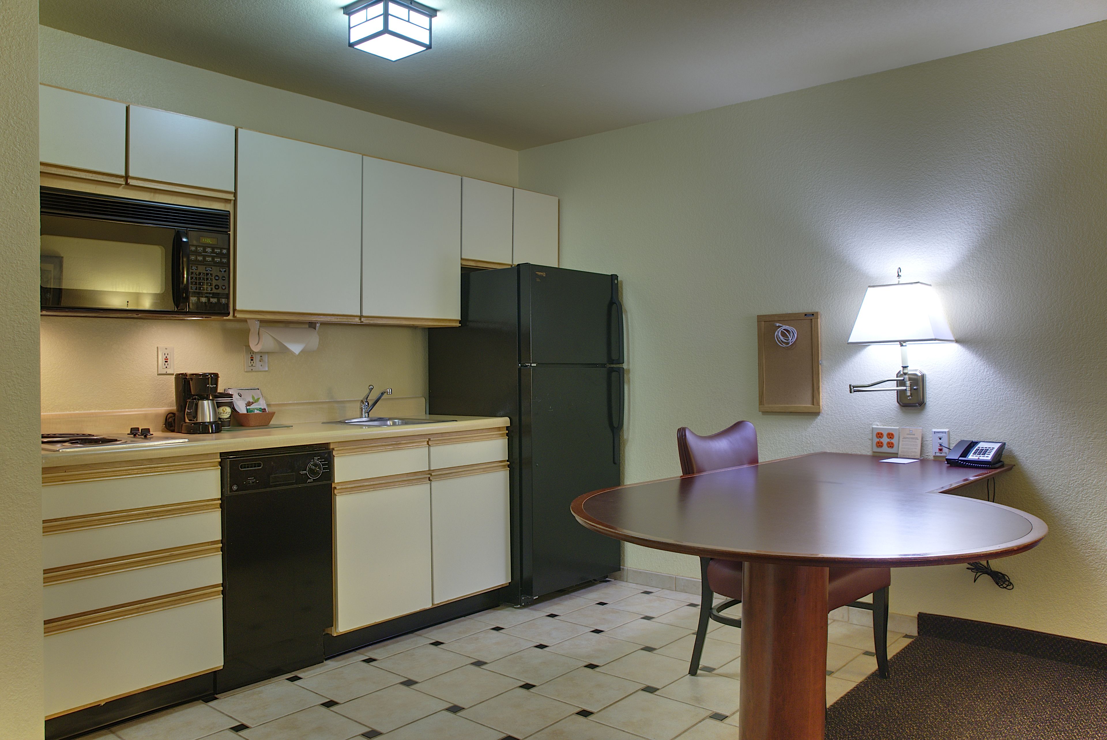 A compact kitchen with a microwave, refrigerator, and dishwasher. There's a small table with chairs and a lamp on the wall.