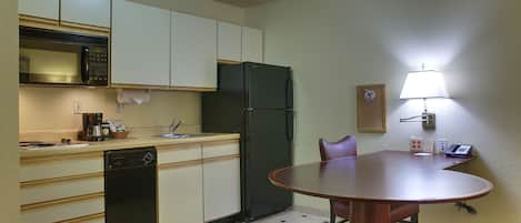 A compact kitchen with a microwave, refrigerator, and dishwasher. There's a small table with chairs and a lamp on the wall.