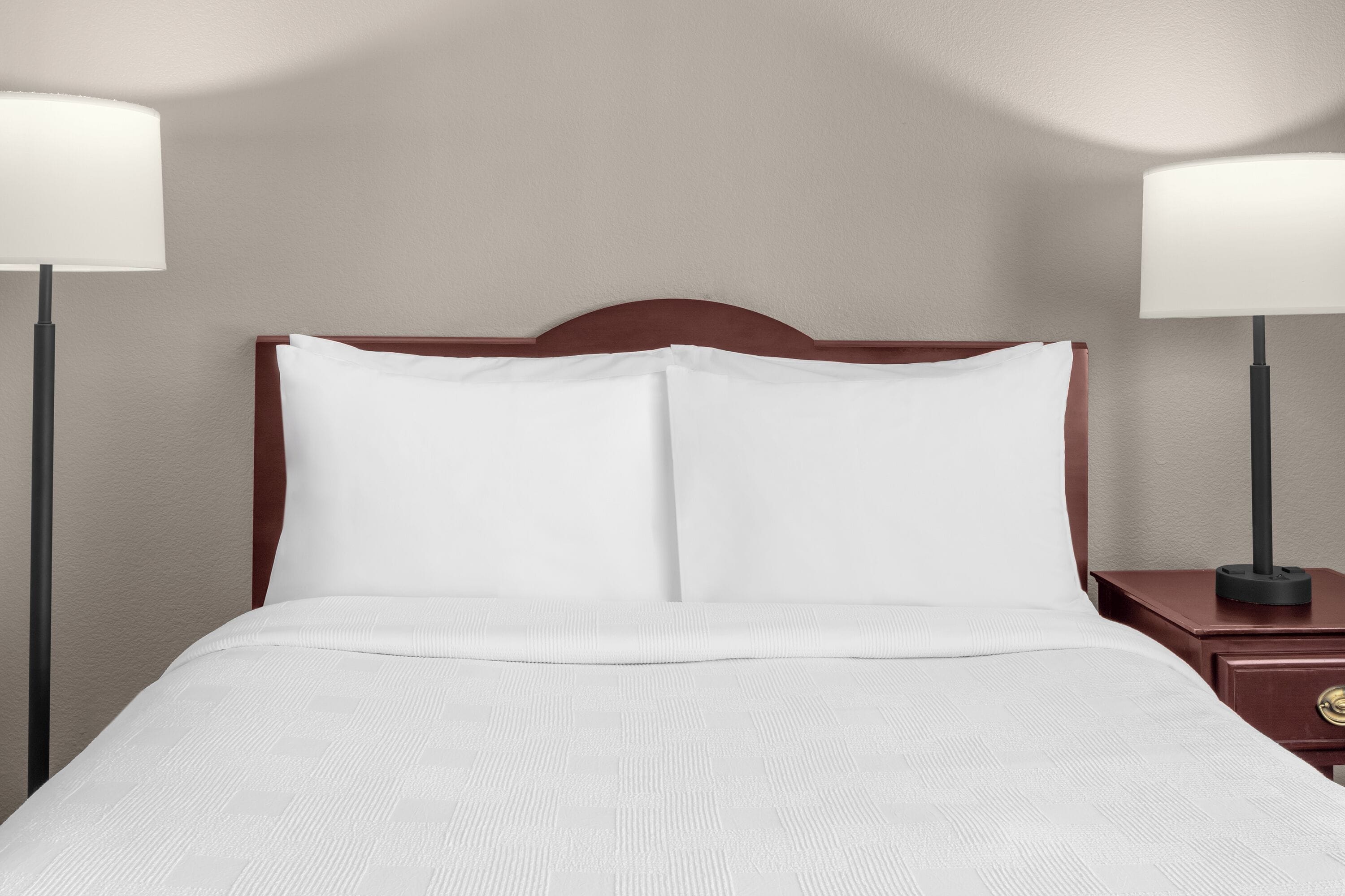 Una cama bien hecha con sábanas blancas, un cabecero de madera y dos lámparas de noche a cada lado.