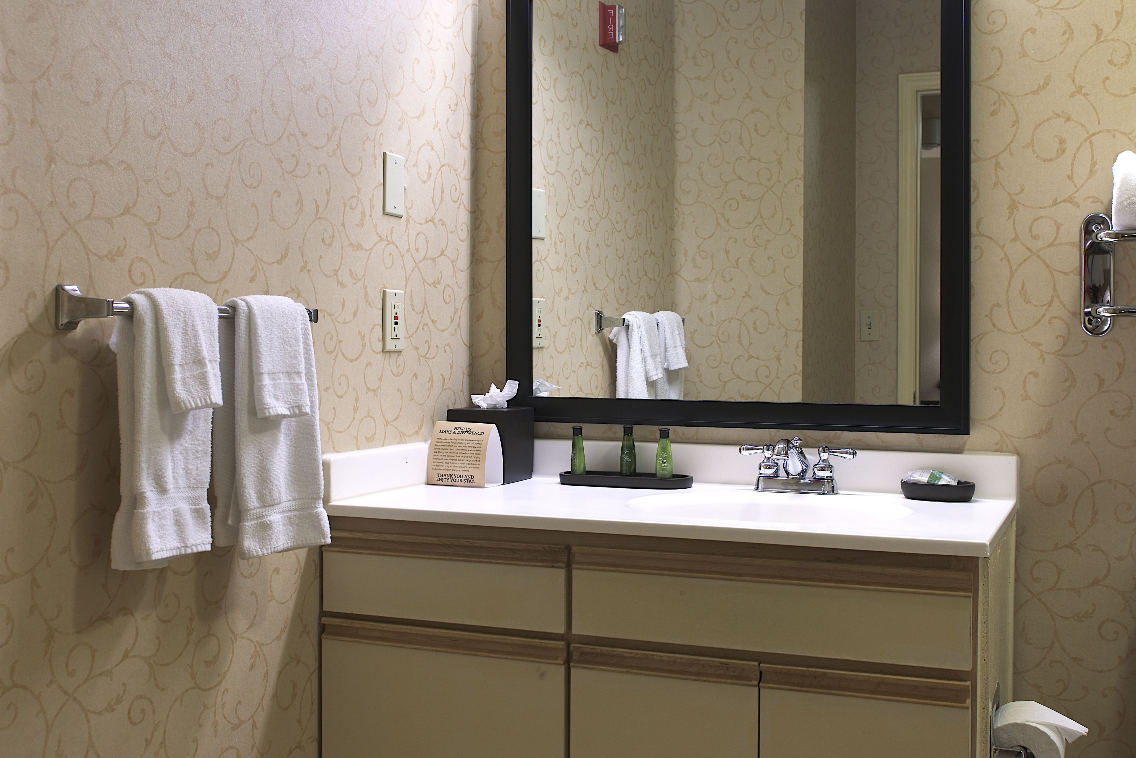 A bathroom with a white sink, a mirror, and two towel racks with towels.