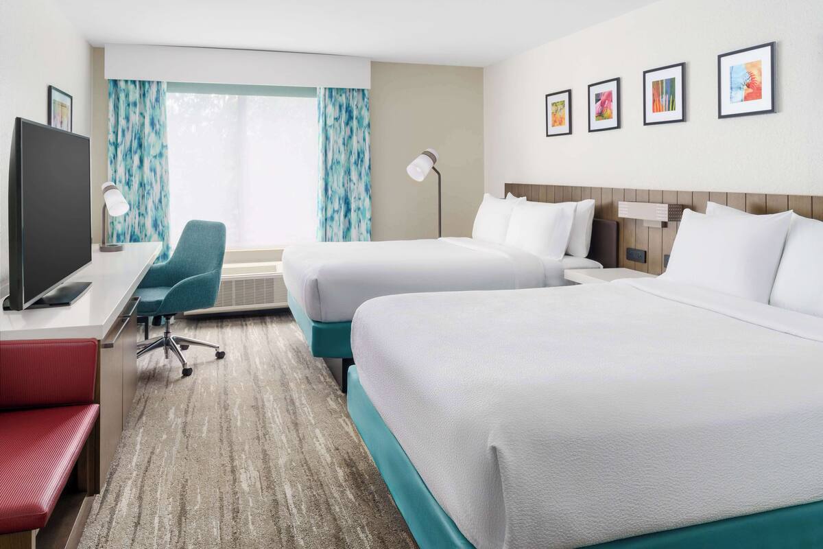 A hotel room with two beds, a desk with a computer, a chair, and a TV.