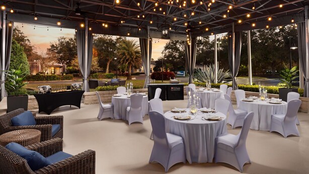 An outdoor dining area with round tables, white tablecloths, and wicker furniture. - Hilton Garden Inn Lake Mary (Lake Mary)
