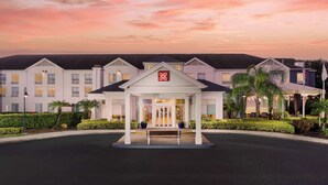 A hotel entrance with a covered waiting area, a bench, and a landscaped garden. - Hilton Garden Inn Lake Mary (Lake Mary)