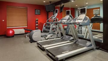 Un gimnasio con cintas de correr, elípticas y una pelota de ejercicios roja.