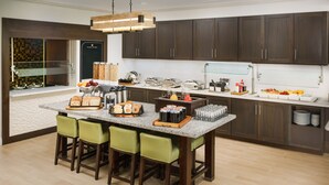 A modern kitchen with dark wood cabinets, a granite countertop, and a central island with bar stools. - Hilton Garden Inn Lake Mary (Lake Mary)