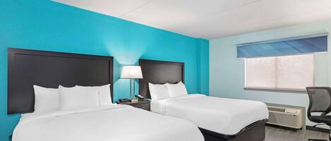Habitación de hotel con dos camas, una mesita de noche, una lámpara, una silla y una ventana con persianas.