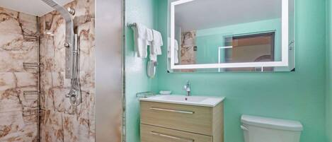 A bathroom with a marble shower, a white sink, a mirror, and a toilet.