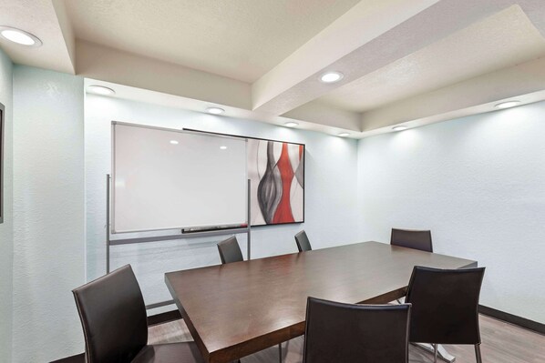 Un salón de conferencias con una gran mesa y seis sillas, una pizarra y un cuadro abstracto moderno en la pared.