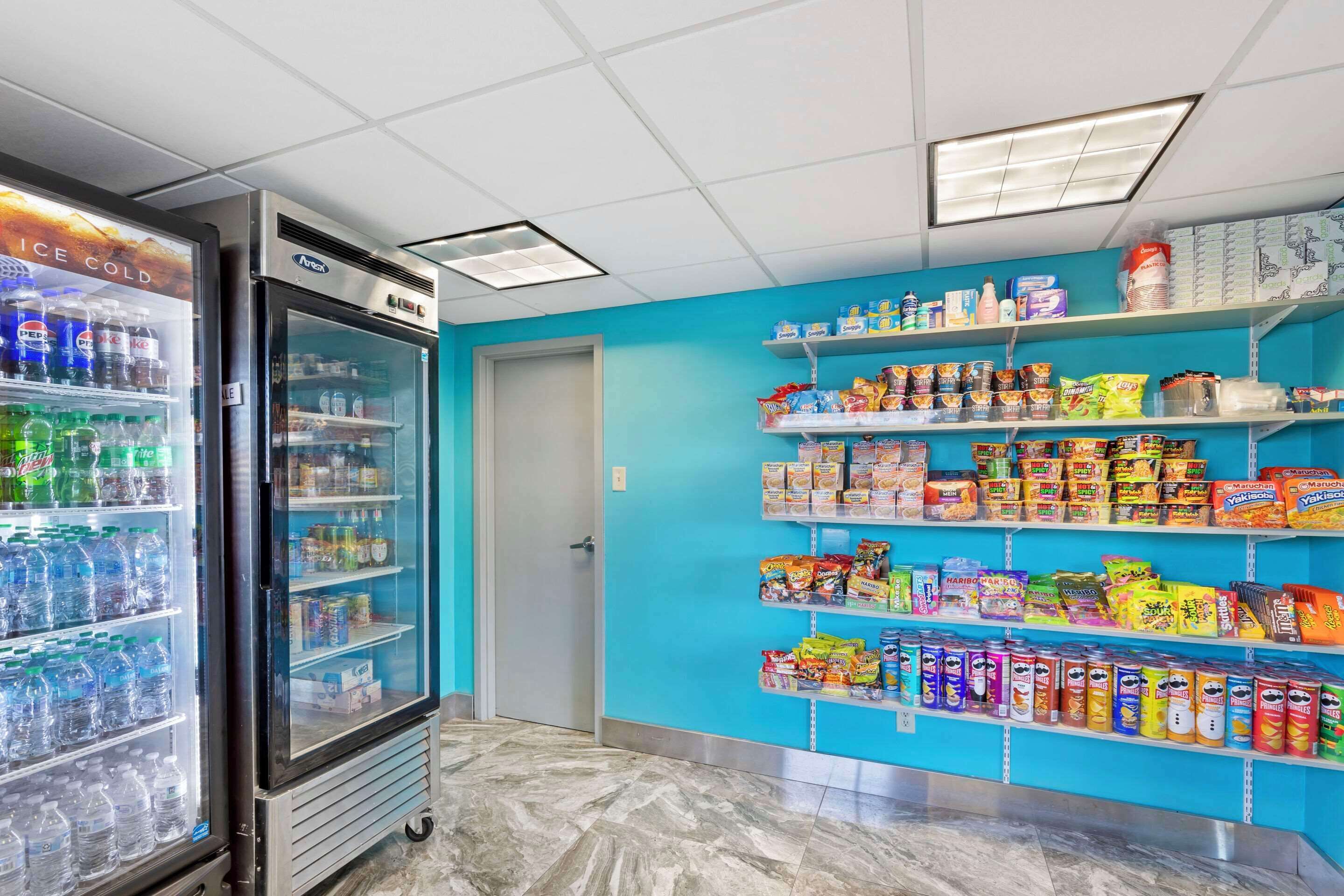 A vending area with a refrigerator and shelves stocked with snacks and beverages.