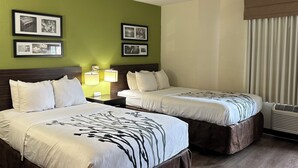 Une chambre d’hôtel avec deux lits, une table de chevet avec des lampes, des tableaux encadrés au mur et un appareil de climatisation.