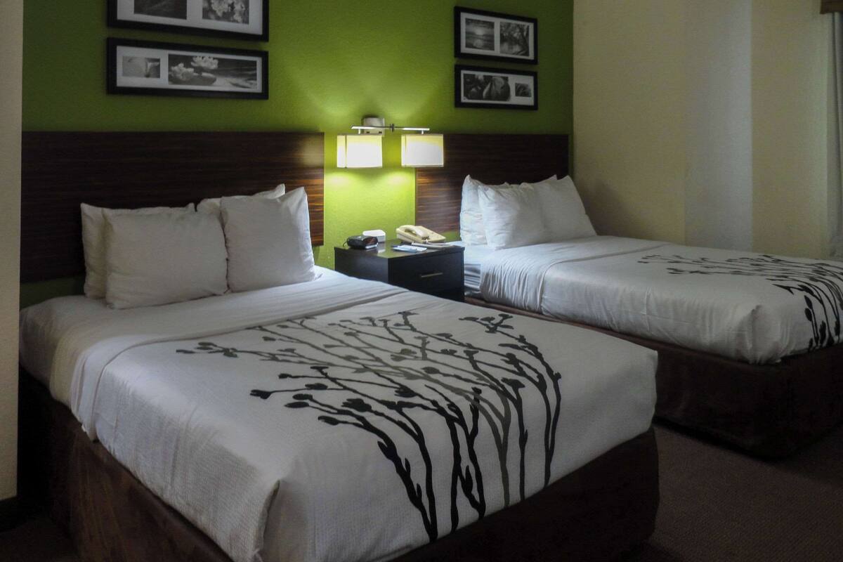A hotel room with two beds, a nightstand with a lamp, and framed pictures on the wall.