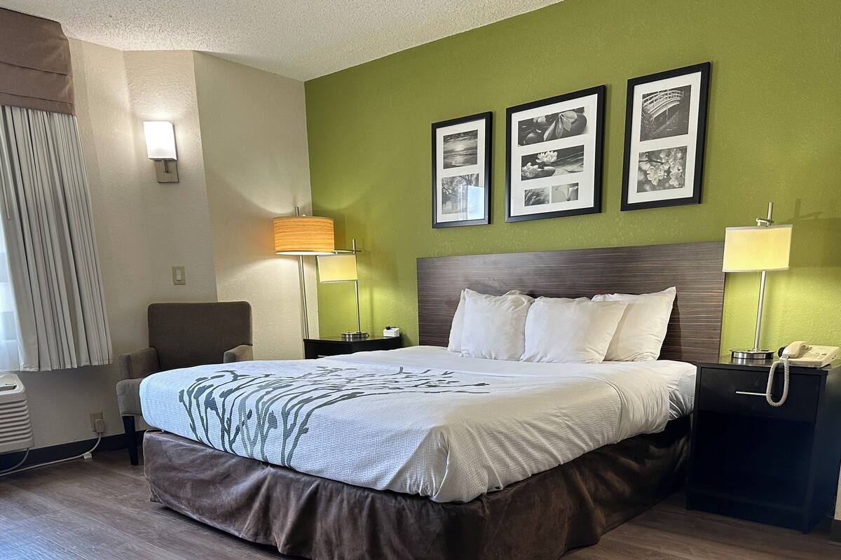 A hotel room with a bed, two bedside tables, a lamp, a chair, and three framed pictures on the wall.
