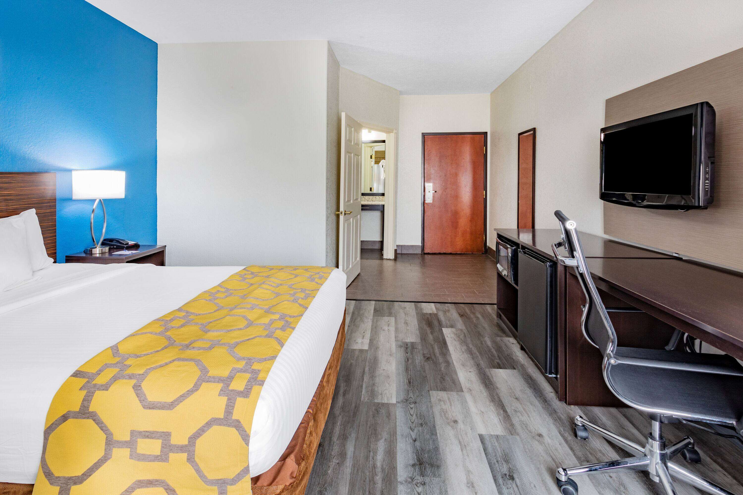A hotel room with a bed, desk, chair, TV, and a bathroom visible through an open door.