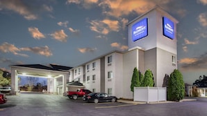 Un hotel con un letrero grande, una zona de estacionamiento techada y una camioneta roja estacionada afuera.