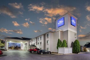 Un hotel con un letrero grande, una zona de estacionamiento techada y una camioneta roja estacionada afuera.