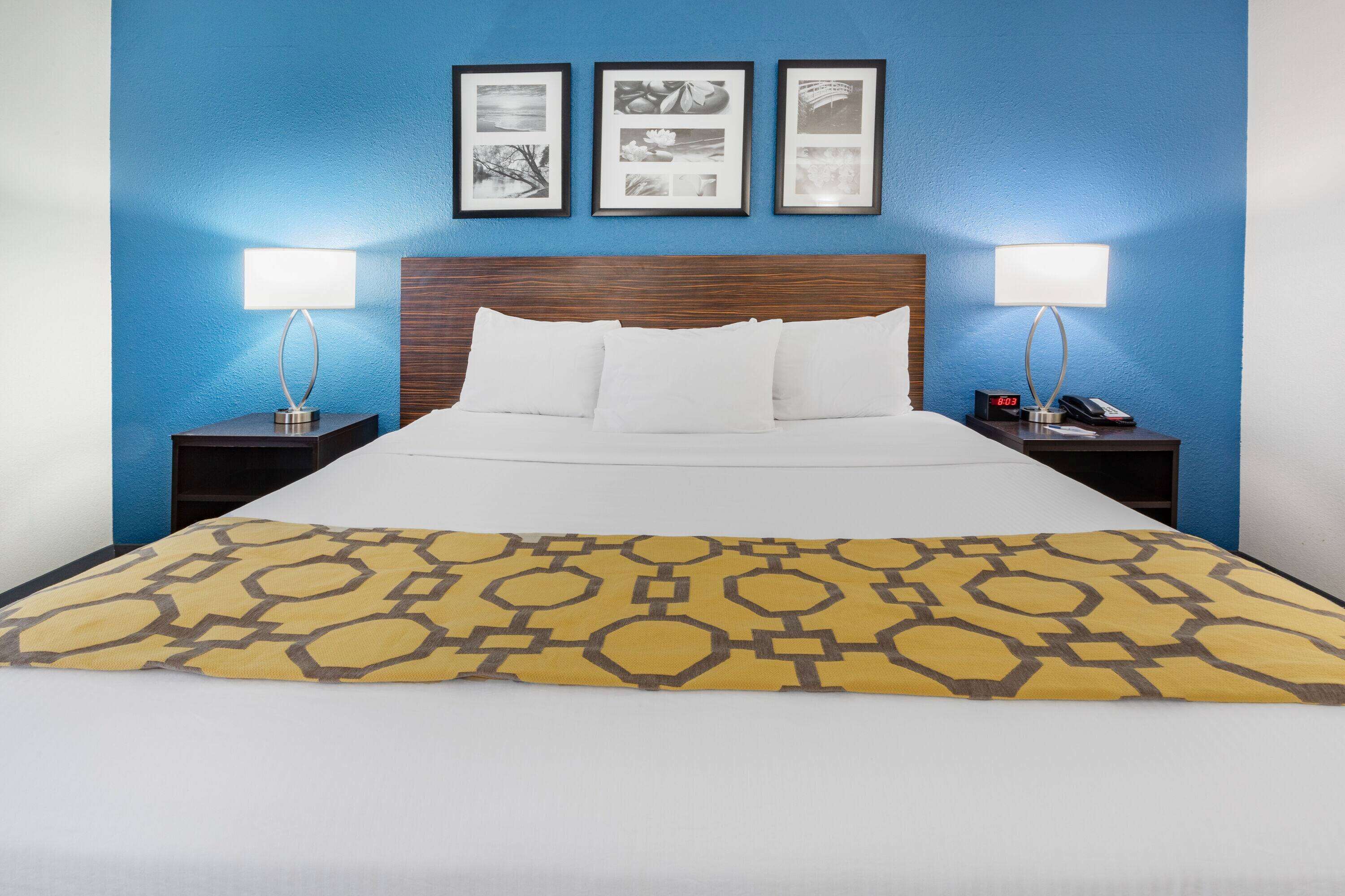 A hotel room with a bed, two bedside tables with lamps, and three framed pictures on the wall.
