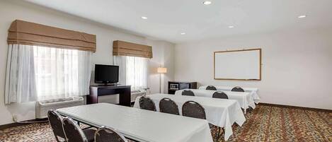 A conference room with a long table, multiple chairs, a television, a whiteboard, and a patterned carpet.