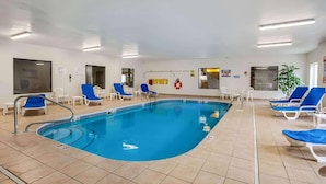 Una piscina interior con agua azul, rodeada de sillones blancos y un suelo de baldosas.