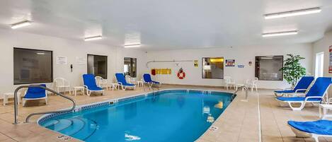Une piscine intérieure à l’eau bleue, entourée de chaises longues blanches et dotée d’un sol carrelé.