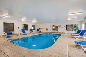 Piscina interior con agua azul, rodeada de sillones blancos y suelo de baldosas.
