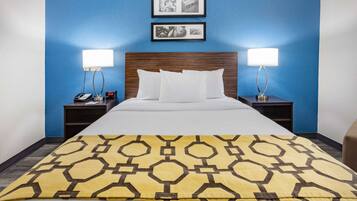 A hotel room with a bed, two bedside tables, a nightstand, a lamp, and a blue wall with two framed pictures.