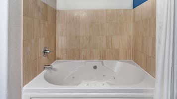 Un baño con una bañera blanca, paredes cubiertas de azulejos color beige y una cortina de ducha blanca.