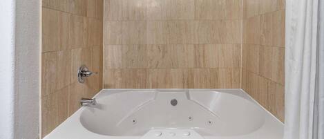 Une salle de bain avec une baignoire blanche, des murs recouverts de carreaux beiges et un rideau de douche blanc.