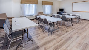 Un salón de conferencias con seis mesas, sillas, una pantalla de proyector y un televisor.