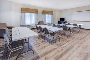 Un salón de conferencias con seis mesas, sillas, una pantalla de proyector y un televisor.