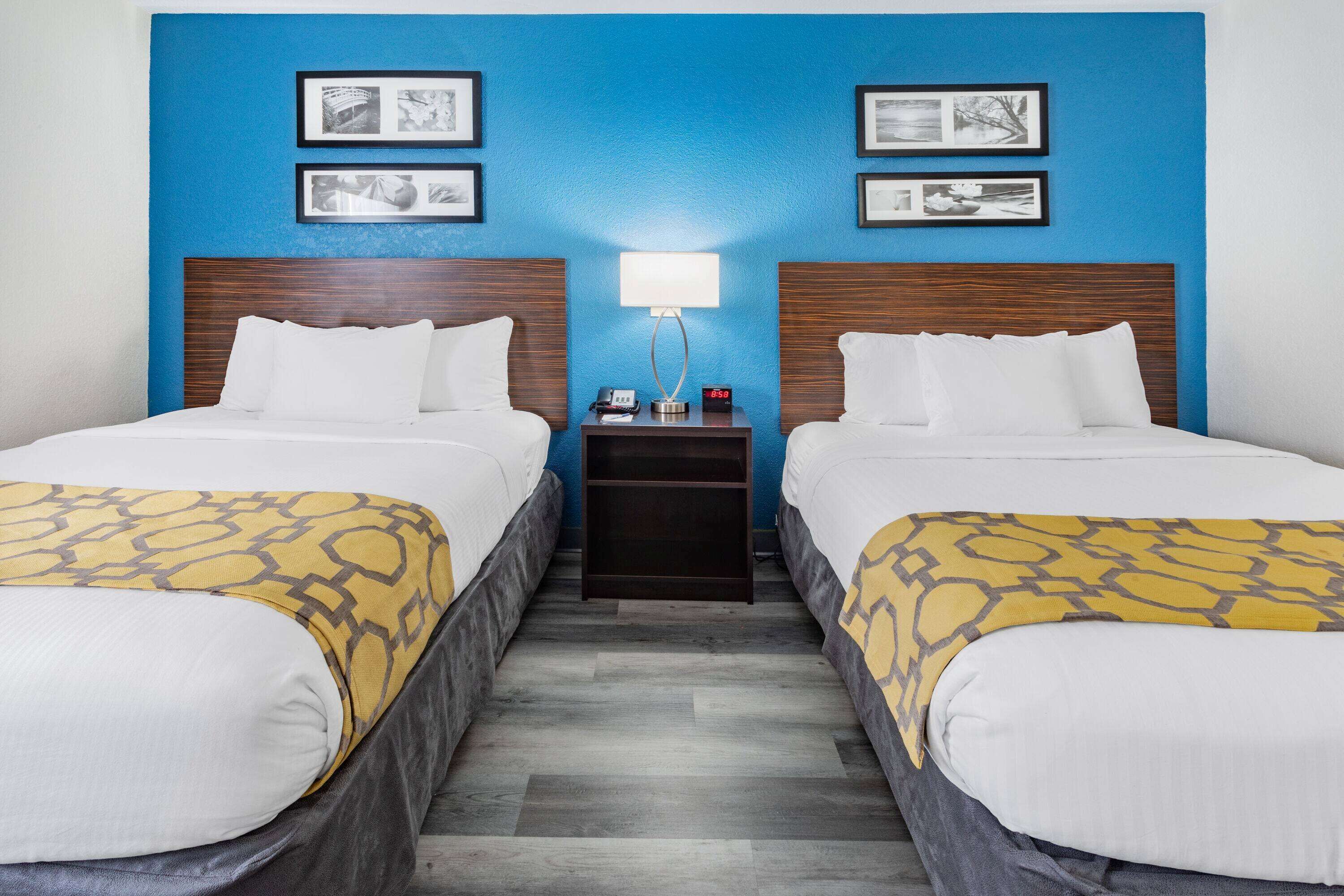 A hotel room with two beds, a nightstand, and a wall with framed pictures.