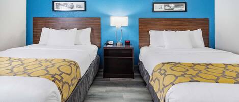 A hotel room with two beds, a nightstand, and a wall with framed pictures.