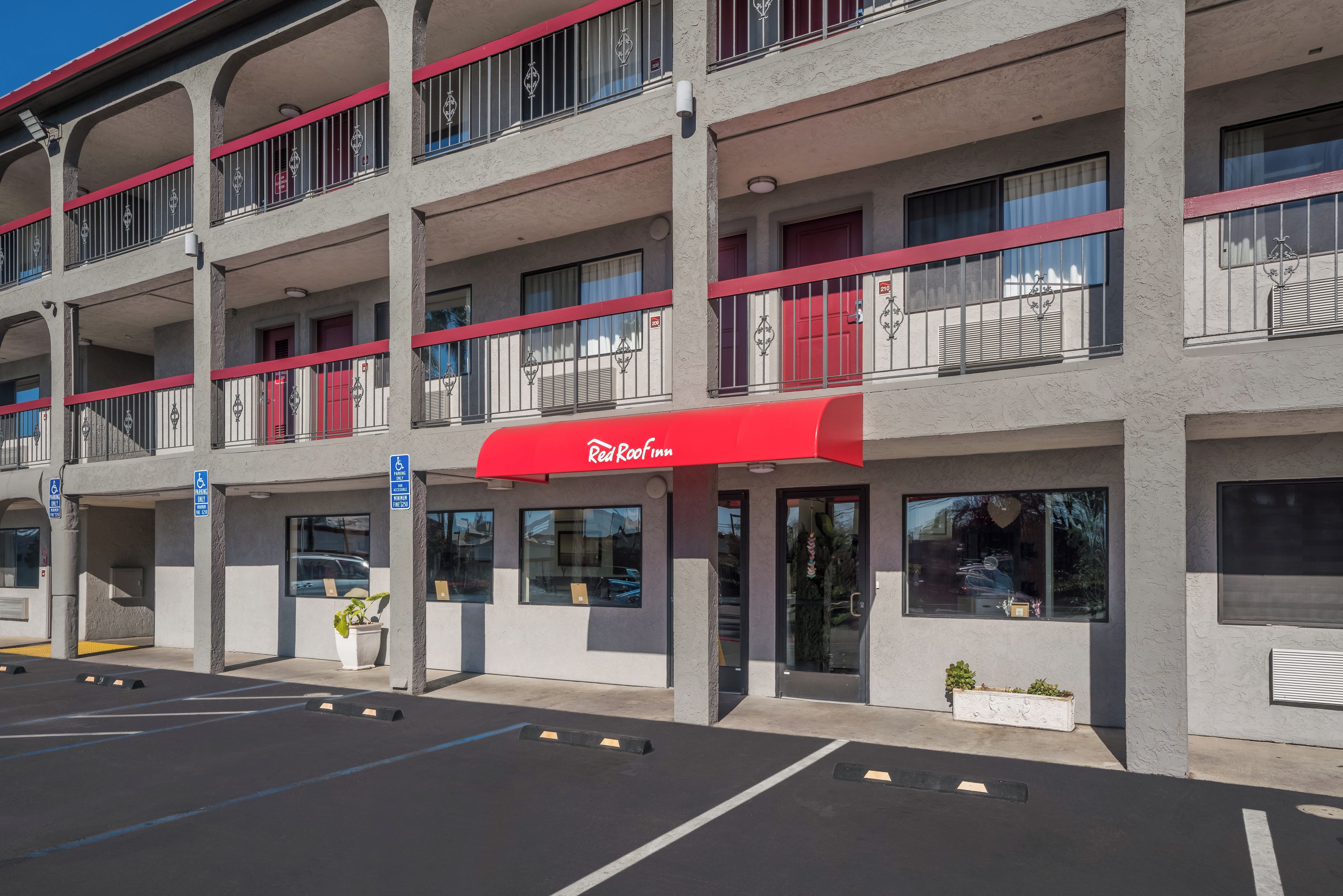 Un edificio de varios pisos con toldo rojo, espacios de estacionamiento y un cartel que indica una zona de estacionamiento para personas con discapacidad.