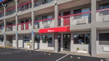 Un edificio de varios pisos con toldo rojo, espacios de estacionamiento y un cartel que indica una zona de estacionamiento para personas con discapacidad.
