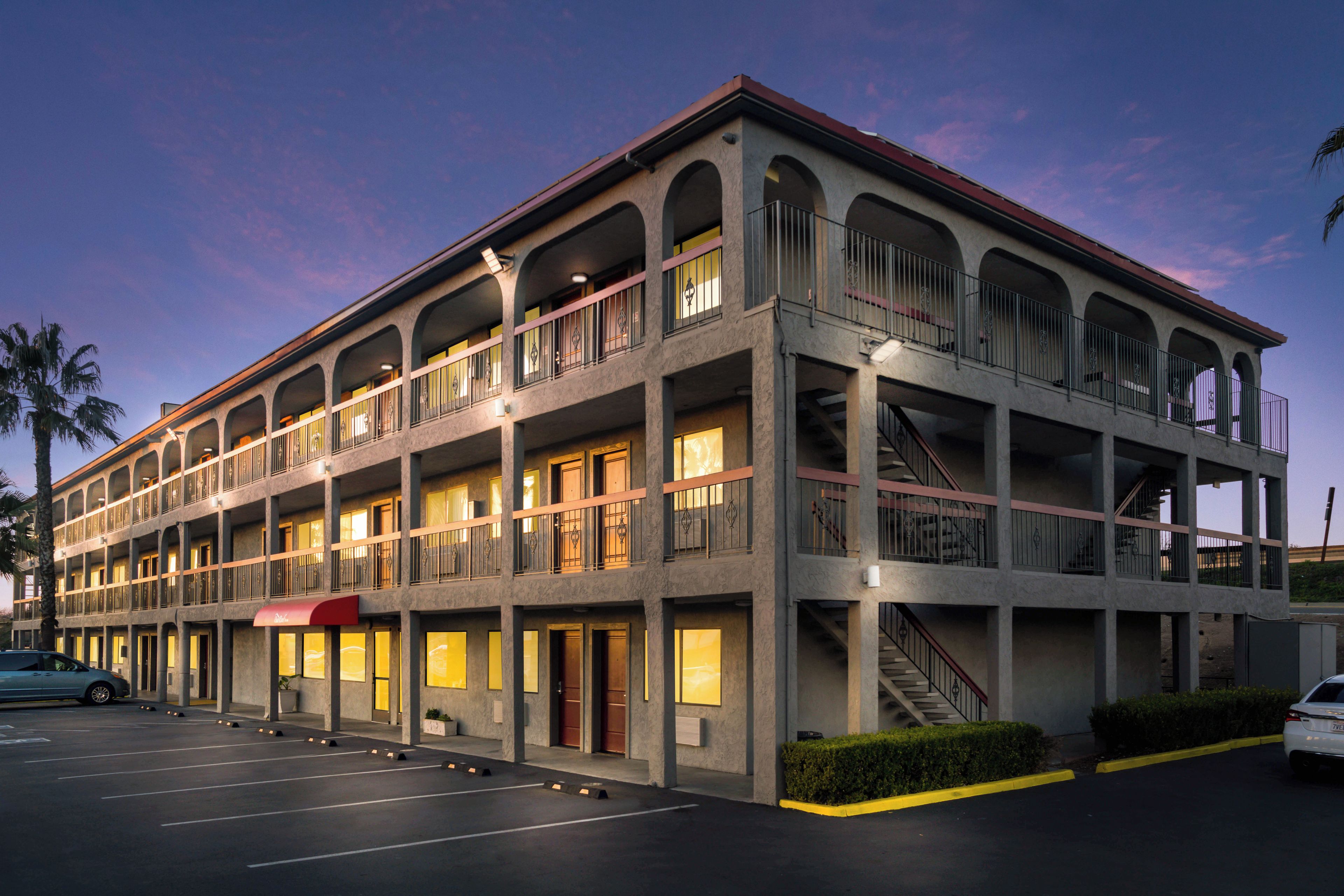 Un hotel de varios pisos con un patio central, balcones y estacionamiento.