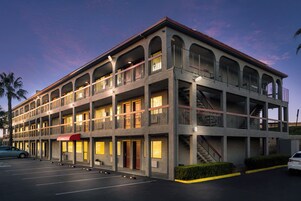 Un hotel de varios pisos con un patio central, balcones y estacionamiento.
