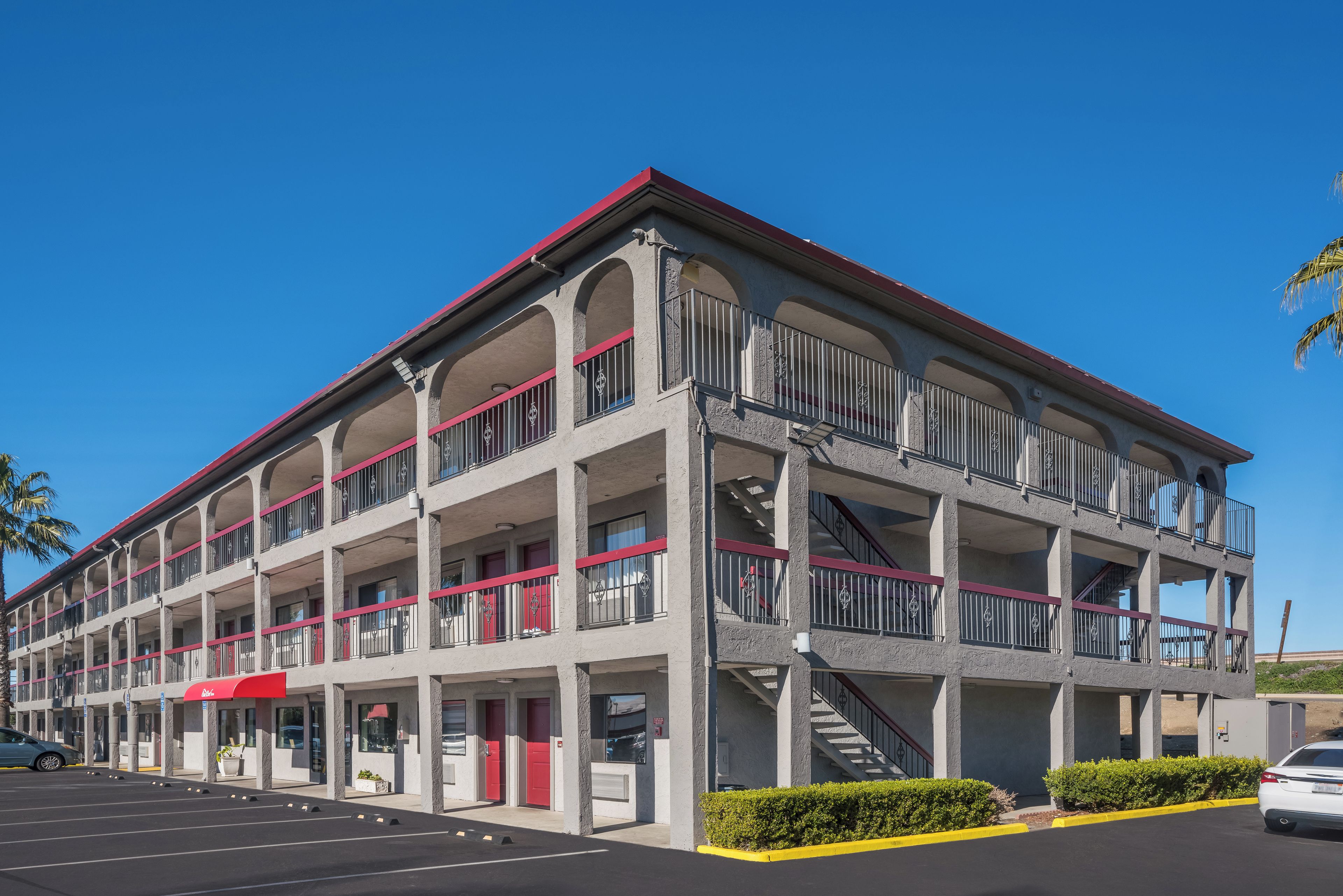 Un edificio de varios pisos con balcones, un toldo rojo y un estacionamiento.