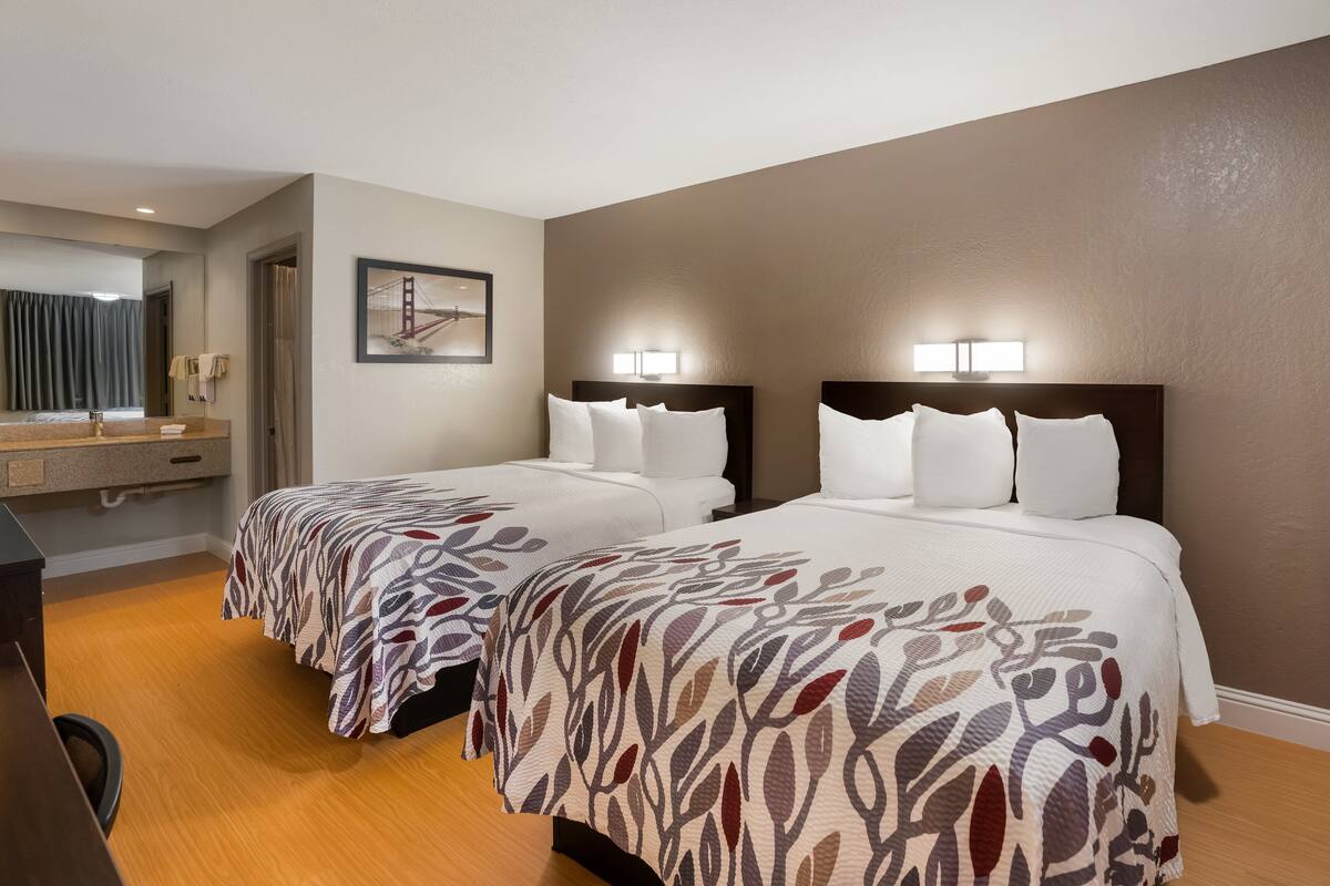 A hotel room with two beds, a desk, and a large window.
