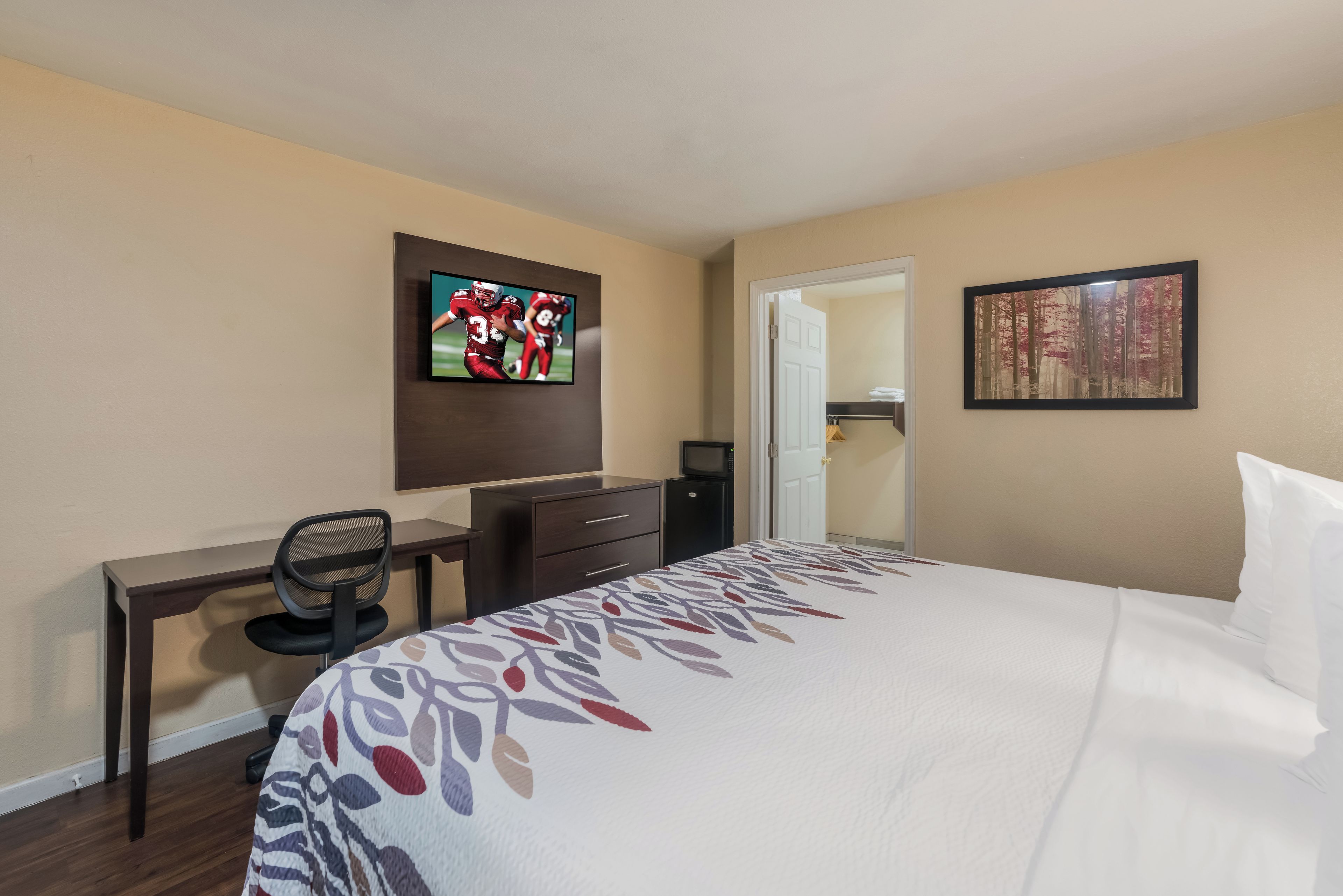 Habitación de hotel con cama, escritorio con silla, televisor en la pared y puerta que da a un armario.