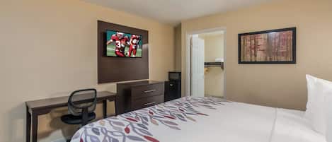 Habitación de hotel con cama, escritorio con silla, televisor en la pared y puerta que da a un armario.