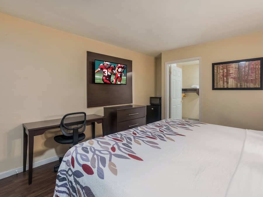 A hotel room with a bed, a desk with a chair, a television on the wall, and a door leading to a closet.