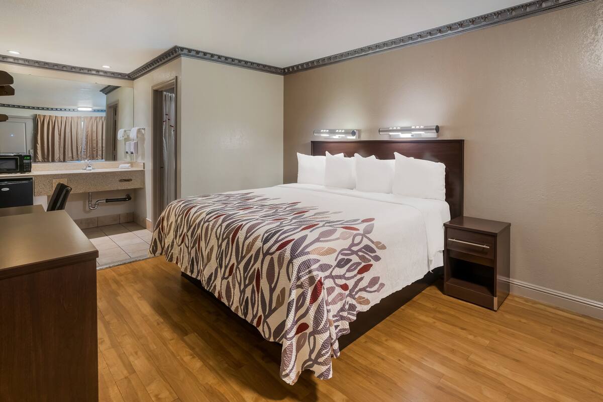 A hotel room with a bed, bedside table, and a desk with a chair.
