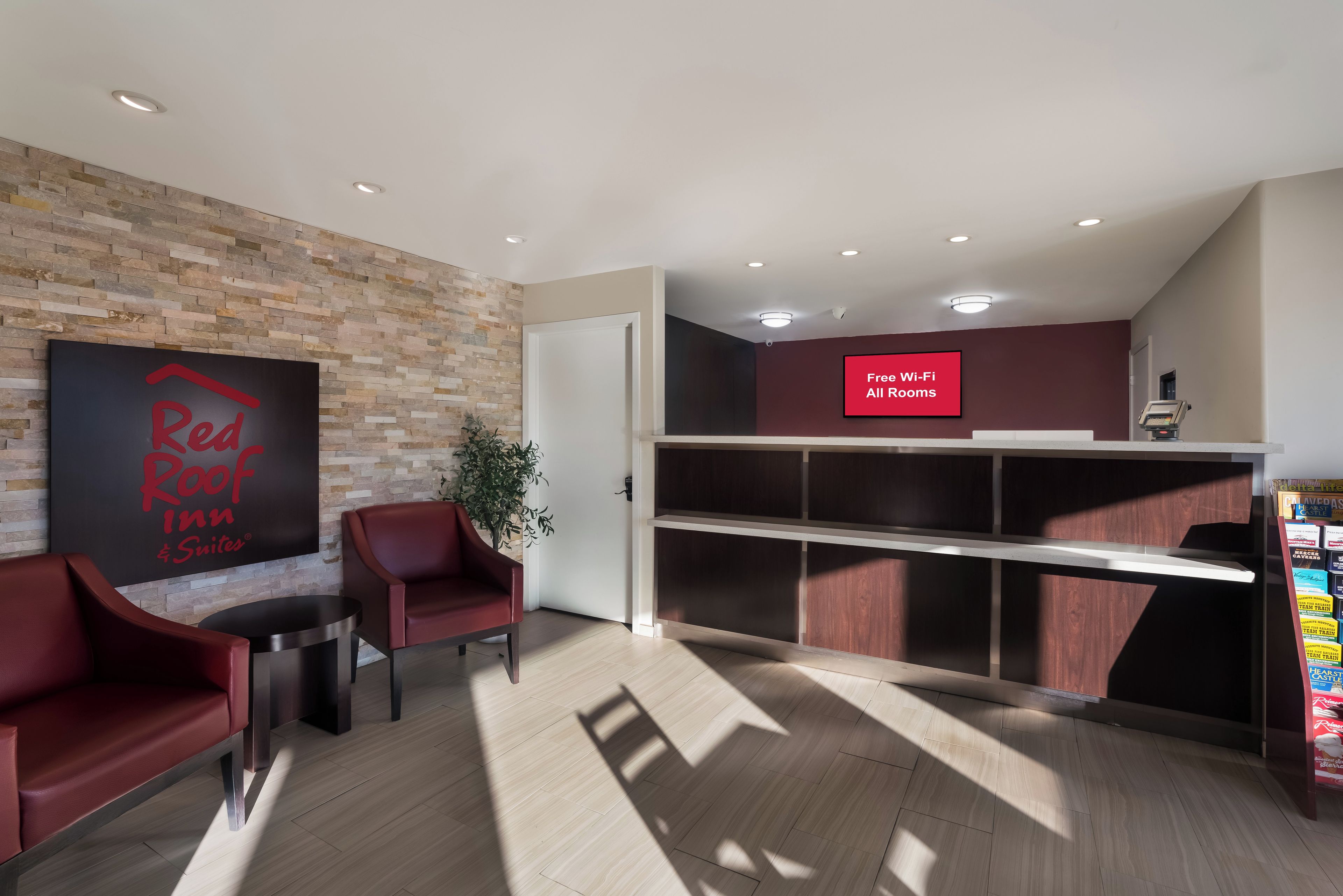 Zona de recepción de hotel con un letrero de Red Roof Inn, un aviso que dice 'Wi-Fi gratuito en todas las habitaciones' y una planta.