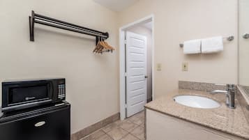 Casa de banho compacta com micro-ondas integrado, uma pia com bancada de granito e um porta-toalhas com ganchos.