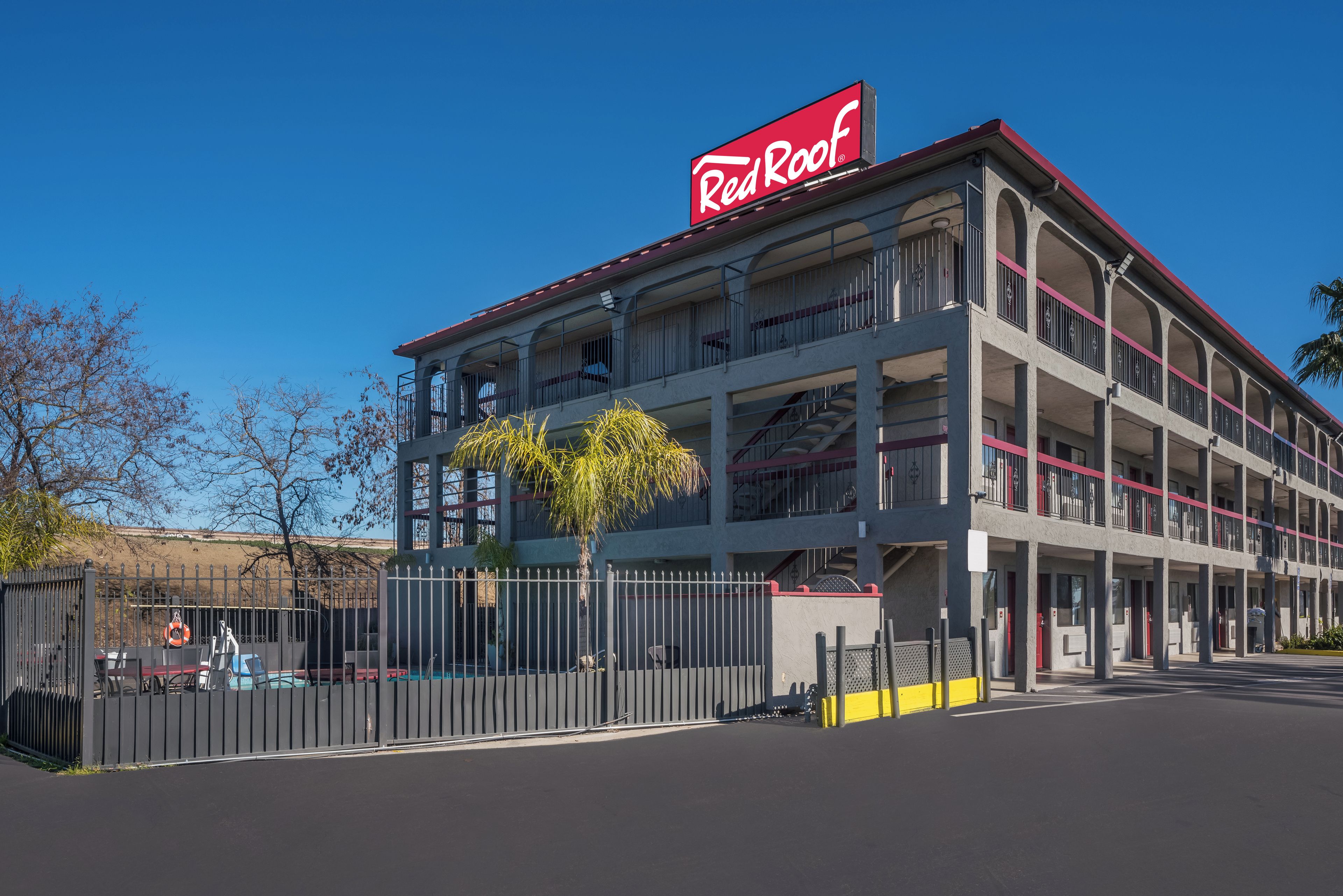 Un edificio de varios pisos con un llamativo letrero de Red Roof, que cuenta con balcones y una entrada con portón.